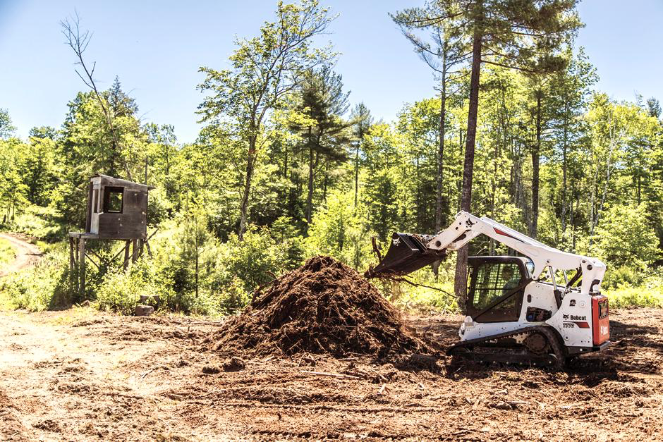 White Bobcat T770 compact track loader with raised bucket beside a soil mound in a wooded clearing