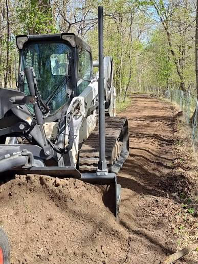 Compact tracked loader grading a dirt driveway in a wooded area
