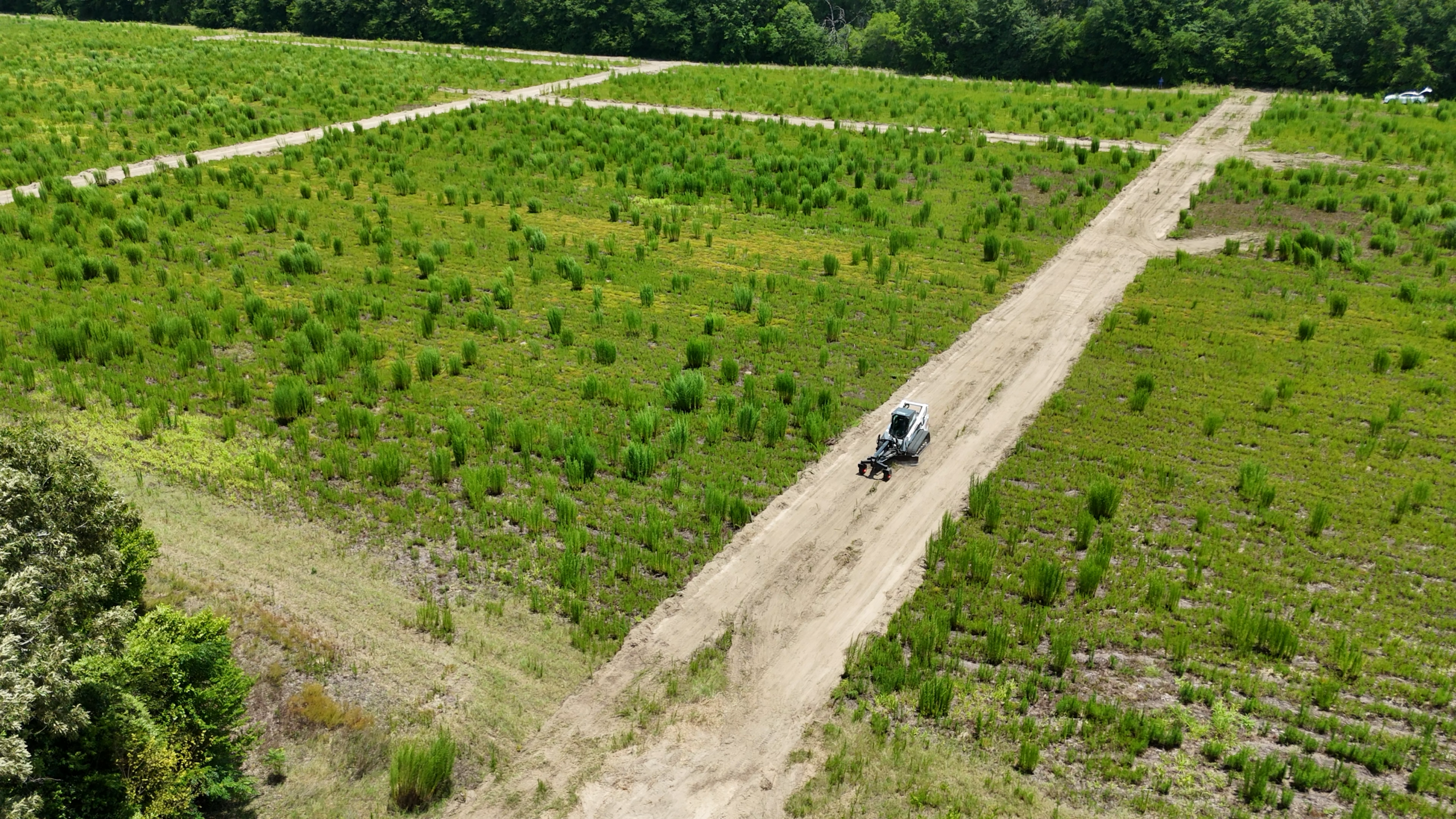 Aerial view of a compact track loader working on a dirt access road through a green field